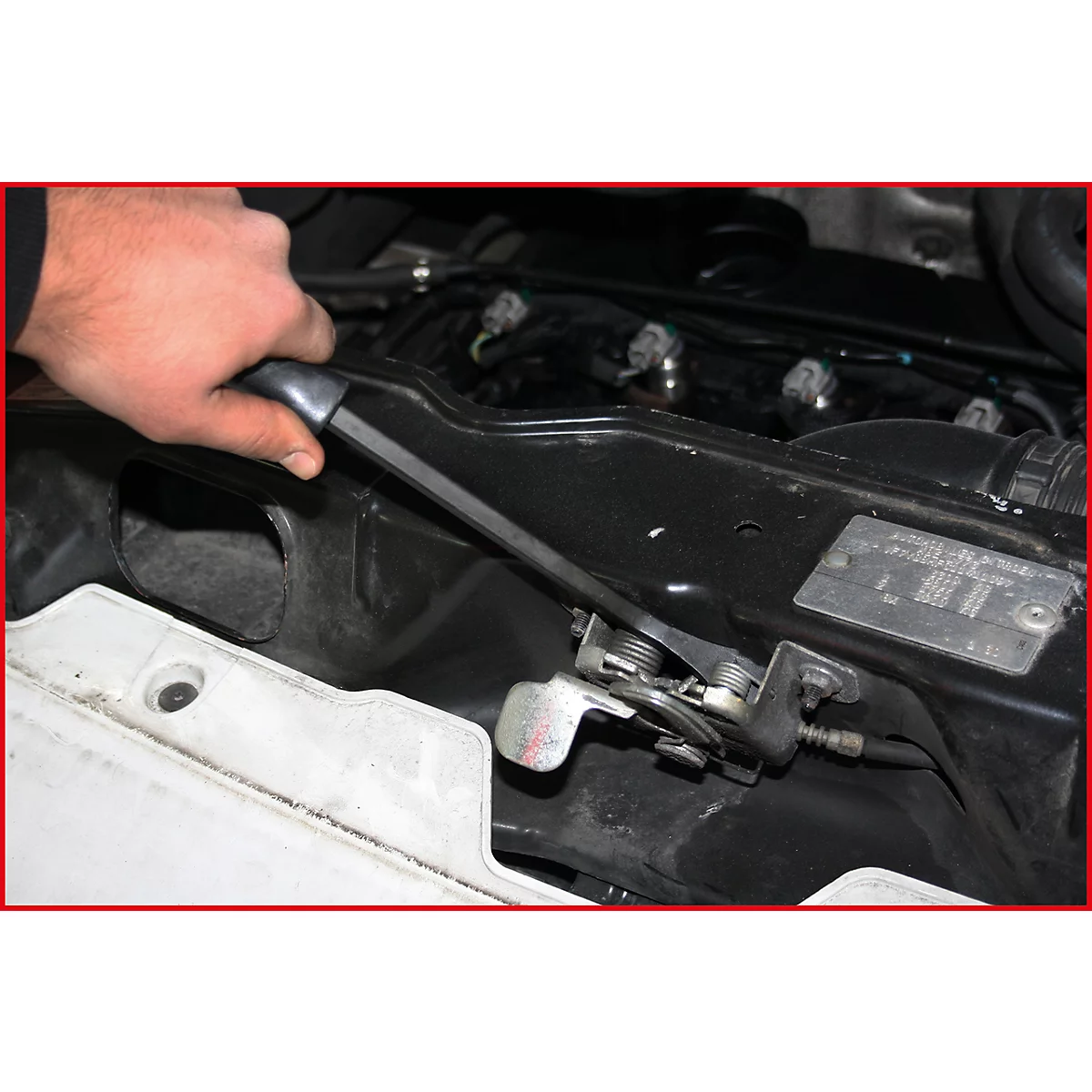 Hand öffnet Motorhaube. Schwarzes Auto mit weißem Kühlergrill, silbernem Hebel und Details des Motors.